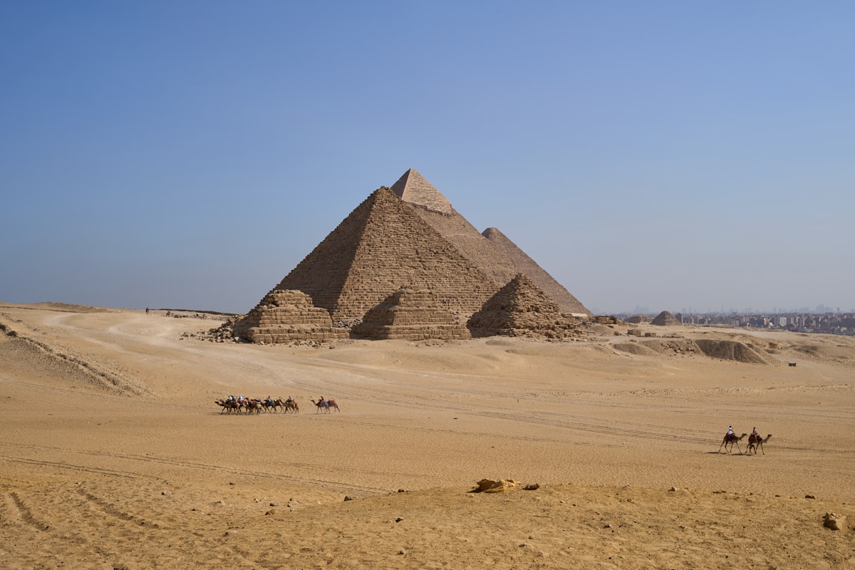 Group of riders on camels crossing the sand plateau in front of the Giza Pyramids, Egypt