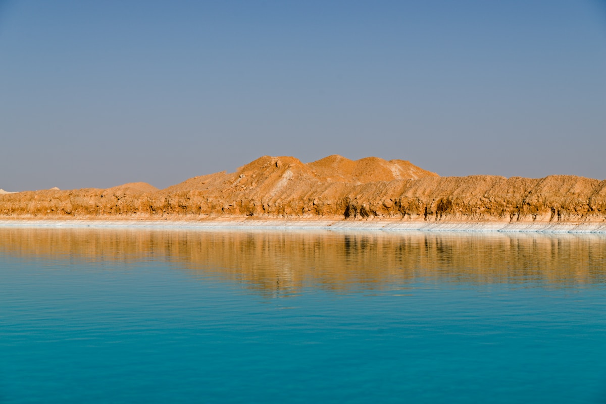 Turquoise salt lake at Siwa Oasis with desert cliffs reflected in still water, Egypt