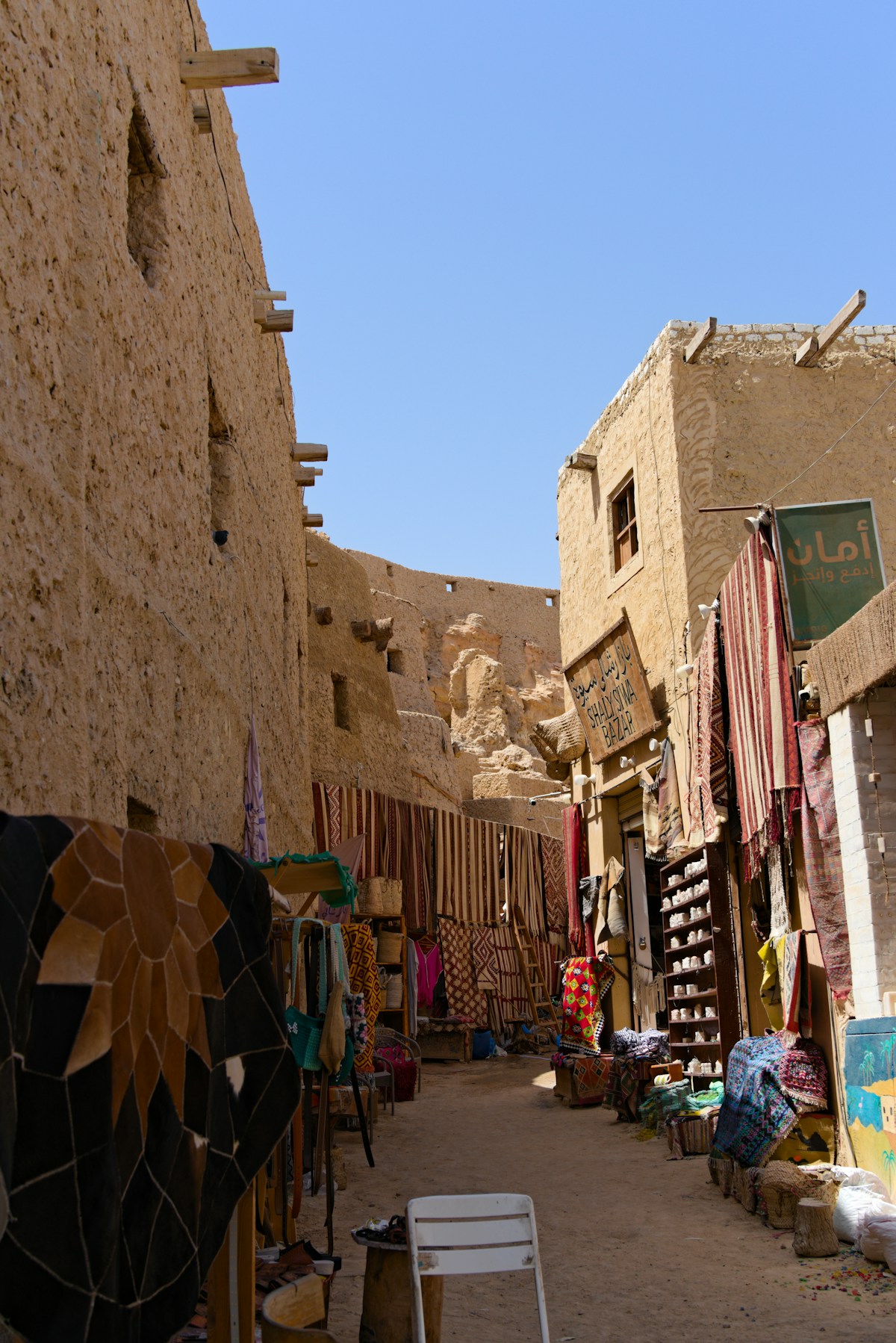 Narrow market alleyway with Arabic signage and textile shops in Siwa, Egypt