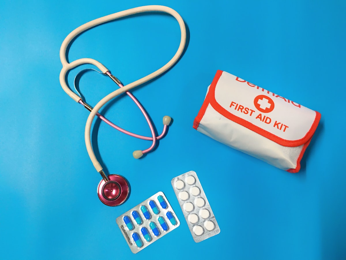 First aid kit with stethoscope and medication blister packs on blue background