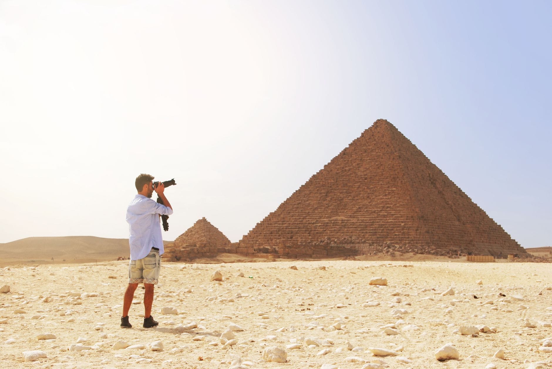 Photographer pointing a camera lens at the Pyramids of Giza in the Egyptian desert