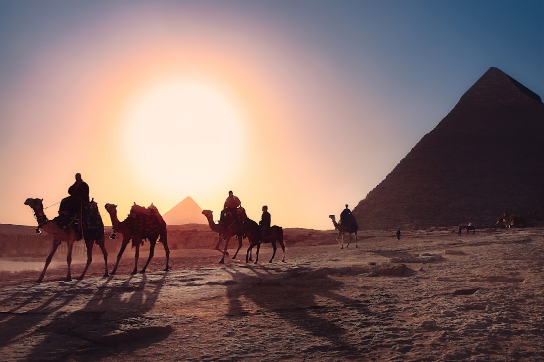 Visiteurs à dos de chameau devant la Grande Pyramide de Gizeh au lever du soleil