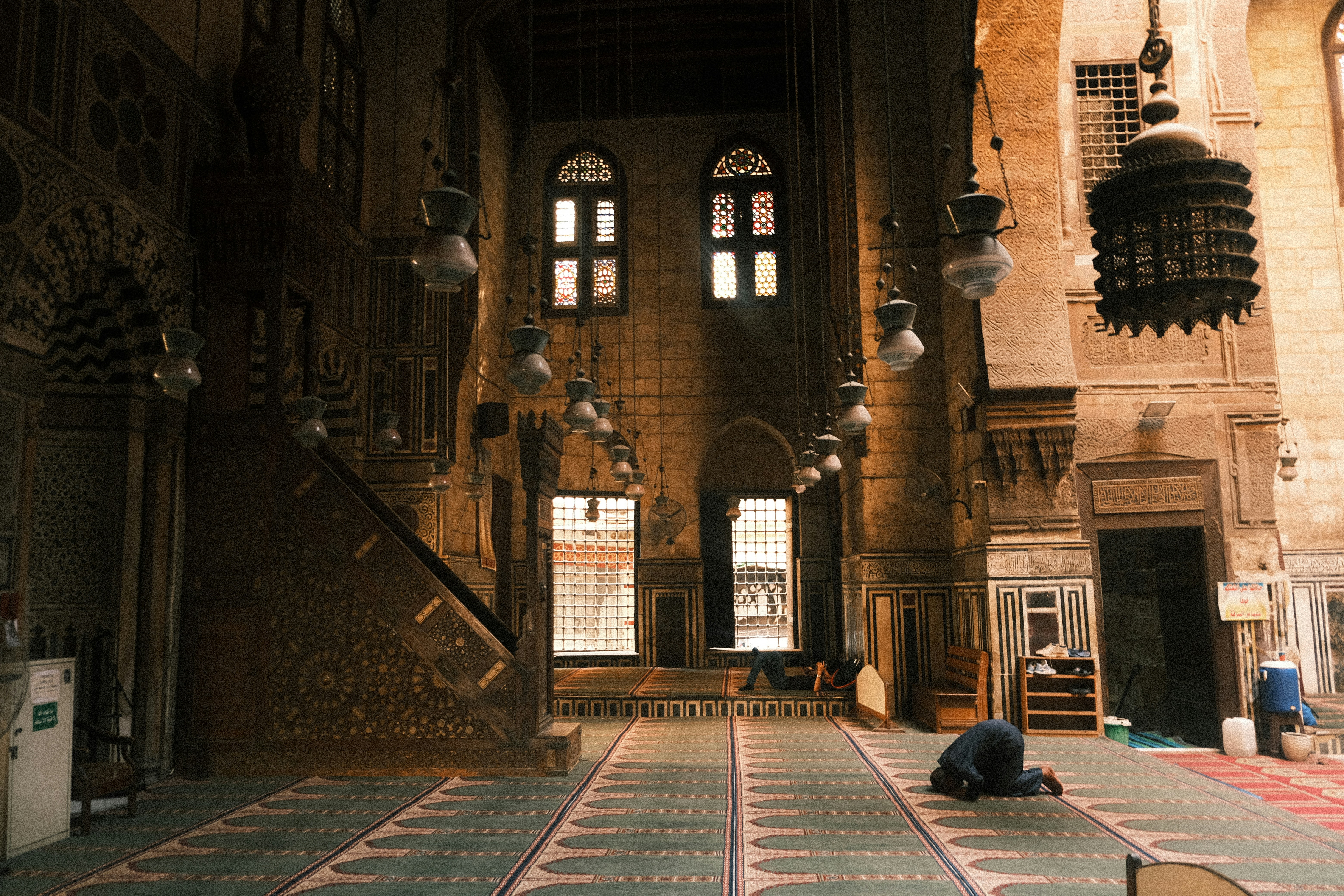 Man praying inside a Cairo mosque with ornate architecture and hanging lanterns