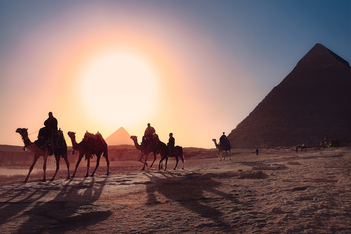 Camel riders silhouetted against a golden sunset at the Pyramids of Giza, Egypt