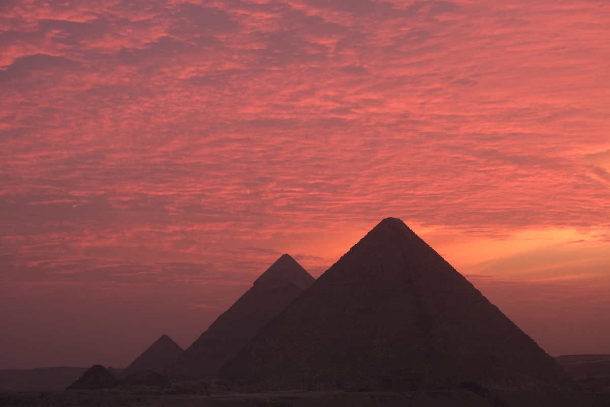 Silhouette of the three Pyramids of Giza against a vivid orange and red sunset sky, Egypt