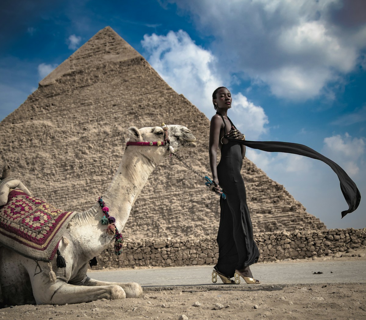 Woman standing next to a camel with the Pyramid of Giza behind her